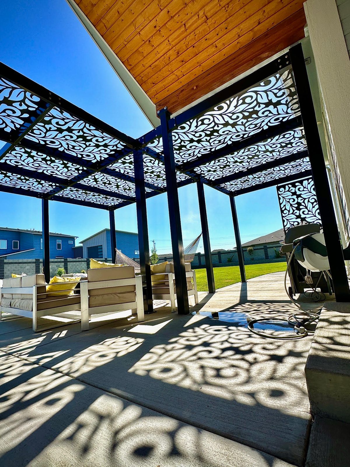 Steel shade structure with ornate laser-cut panels casting patterned shadows across a residential patio